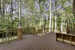 A large wooden deck provides an expansive view of a lush forest, creating a serene and natural atmosphere, perfect for relaxation and outdoor gatherings.